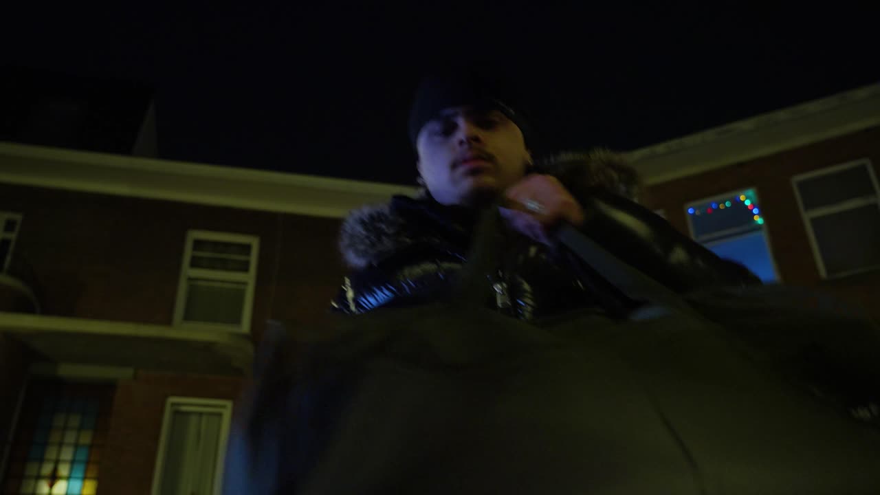 Man met capuchon tussen bakstenen huizen, van onderaf gefilmd bij nacht